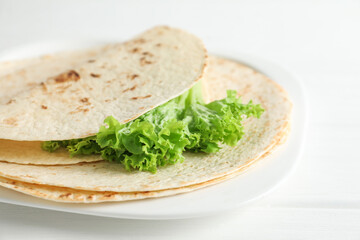 Tasty homemade tortillas and lettuce on white wooden table, closeup