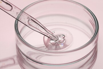 Glass pipette and petri dish with liquid on pink background, closeup
