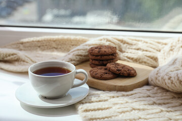 Beige knitted scarf, tea and cookies on windowsill, closeup