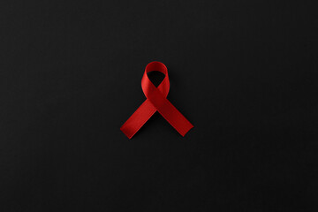 Red awareness ribbon on black background, top view