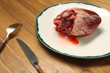 Raw heart, fork and knife on wooden table