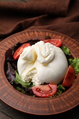 Fresh delicious burrata salad in bowl on table, closeup