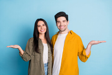 Photo of two nice young partners hold empty space vs wear shirt isolated on blue color background