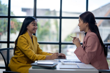 Two women are sitting at a desk, one of them is smiling