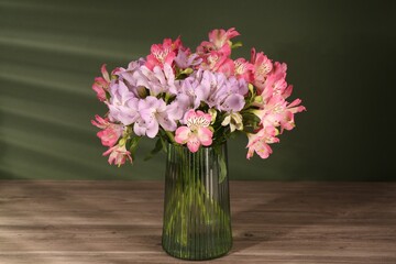 Beautiful alstroemeria flowers in vase on wooden table against green background