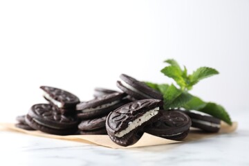 Tasty sandwich cookies and mint on white marble table