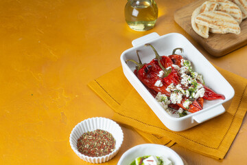 Grilled red pepper with feta cheese and olive oil on white tray on yellow background.