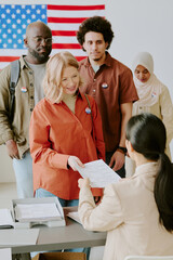 Vertical medium long shot of ethnically diverse men and women standing in line at voting place...