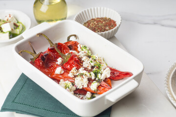 Summer healthy tasty Mediterranean cuisine concept. Sweet red roasted peppers salad with extra virgin olive oil and feta cheese on white tray top view, close-up