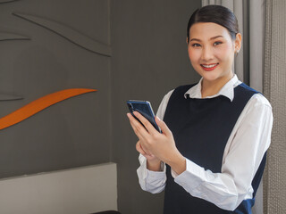 Asian woman chambermaid in uniform speaking on room telephone during work. She smiles and looking at the camera takes orders from the hotel administrator.