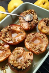 Tasty baked quinces with nuts and honey in dish on grid, closeup