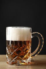 Mug with fresh beer on wooden table against black background