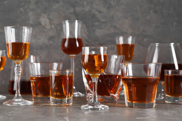 Different delicious liqueurs in glasses on grey table