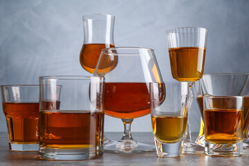 Different liqueurs in glasses on grey table, closeup