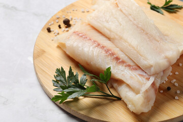 Pieces of raw cod fish, spices and parsley on white marble table, closeup