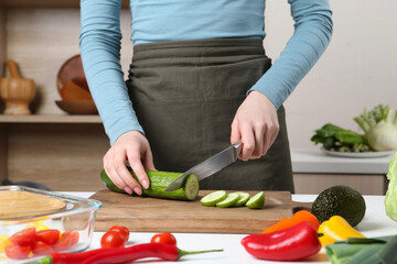 Healthy food. Woman cutting cucumber at white table in kitchen, closeup