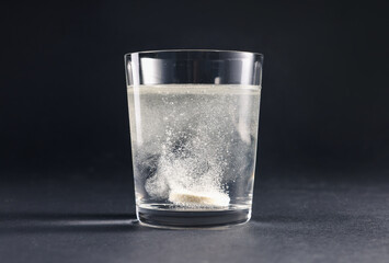 Effervescent pill dissolving in glass of water on grey table