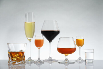 Glasses with different alcoholic drinks on white table against light background