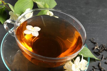 Aromatic jasmine tea in glass cup, flowers and dry leaves on grey table, closeup