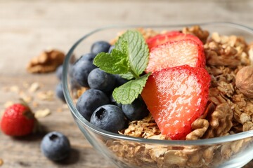 Tasty granola with berries, nuts and mint on wooden table, closeup