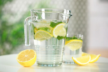 Refreshing lemonade with mint in jug and glass on white table, closeup