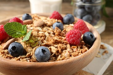 Tasty granola with berries, nuts and mint on wooden table, closeup