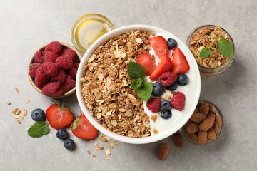 Tasty granola with berries and yogurt in bowl on grey textured table, flat lay