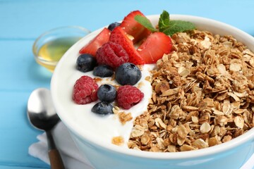 Tasty granola with berries and yogurt in bowl on light blue table, closeup