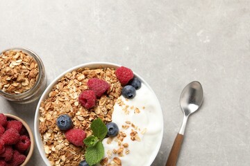 Tasty granola with berries and yogurt served on grey textured table, flat lay. Space for text