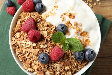 Tasty granola with berries and yogurt in bowl on wooden table, top view