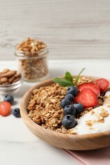 Tasty granola with berries and yogurt in bowl on white table, closeup