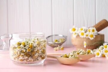 Chamomile flowers in glass jar and spoons on pink wooden table
