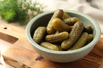 Pickled cucumbers in bowl on wooden board, closeup