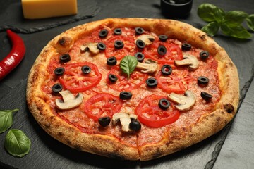 Delicious pizza with tomatoes, mushrooms, olives and basil on black table, closeup