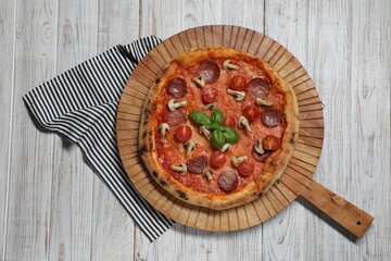 Delicious pizza with salami, tomatoes, mushrooms and basil on wooden table, top view
