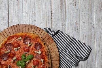 Delicious pizza with salami, tomatoes, mushrooms and basil on wooden table, top view. Space for text