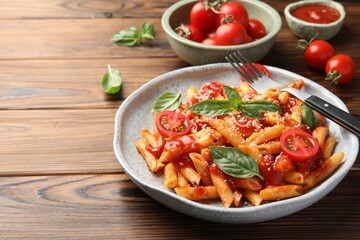 Delicious pasta with tomato sauce, basil and cheese served on wooden table, closeup. Space for text