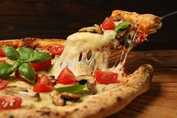 Taking piece of tasty pizza with melted cheese at wooden table, closeup