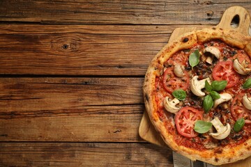 Tasty pizza with basil, mushrooms and tomato on wooden table, top view. Space for text