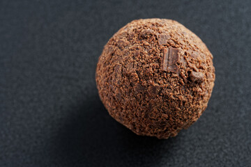 Delicious chocolate candy - a ball sprinkled with chocolate chips. Dark background. Photo. Macro. Selective focus. Copy space