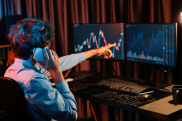 Young business trader calling to broker, consulting profit currency rate investment on global market online on pc screen in real time at neon light modern office. Concept of stock exchange. Gusher.