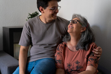 A mother and her adult son sitting together on a couch, looking at each other with warm smiles