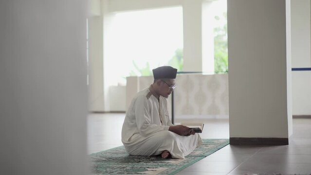 A young asian muslim reading koran in the mosque. Muslims will do this activity more often in the month of Ramadan