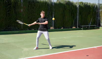 Young tennis player hitting tennis ball on outdoor court