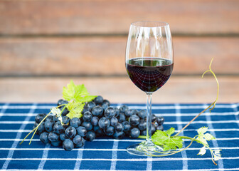 Delicious red wine and ripe grapes on a checkered blue table close in the summer cottage garden.  Red natural wine, bunch of grapes in a garden in nature.