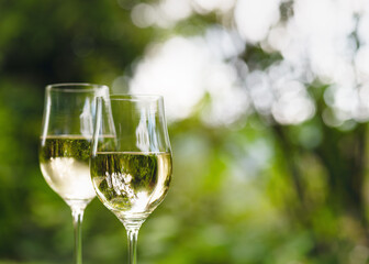 Two wine glasses with white wine and a beautiful bokeh on the background. The focus is on the reflection in the wine glass. Shallow depth of field. Copy space.
