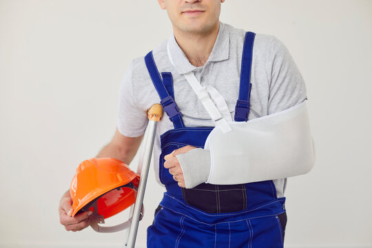 Workplace career trauma, workplace accident, bad job insecurity, traumatic event in building, male builder in professional workwear overall, hard hat with broken arm support, crutches, life insurance 