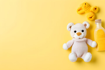The image shows a knitted teddy bear wearing a yellow scarf, sitting next to a yellow baby bottle on a bright yellow background. 
