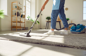 Cropped photo of woman cleaning with vacuum cleaner carpet in the living room at home. Female...
