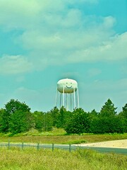 Smiley water tank tower on a nice sunny day  surrounded by wild landscape trees and shrubs.